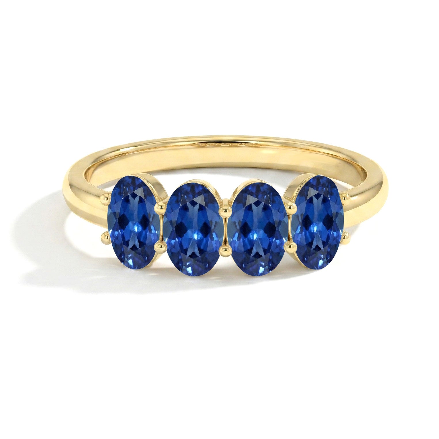 A yellow gold ring featuring four oval-cut deep blue gemstones in a row, set against a clean white background.