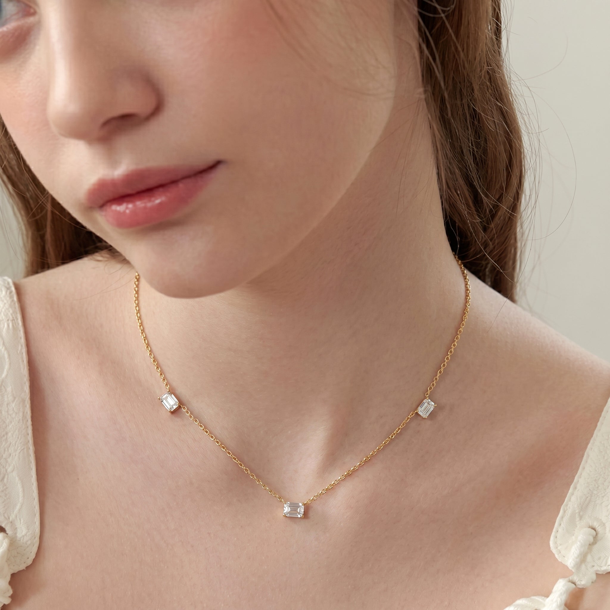 A close-up of a model wearing a delicate chain necklace with three small light blue rectangular gemstones spaced along the chain.
