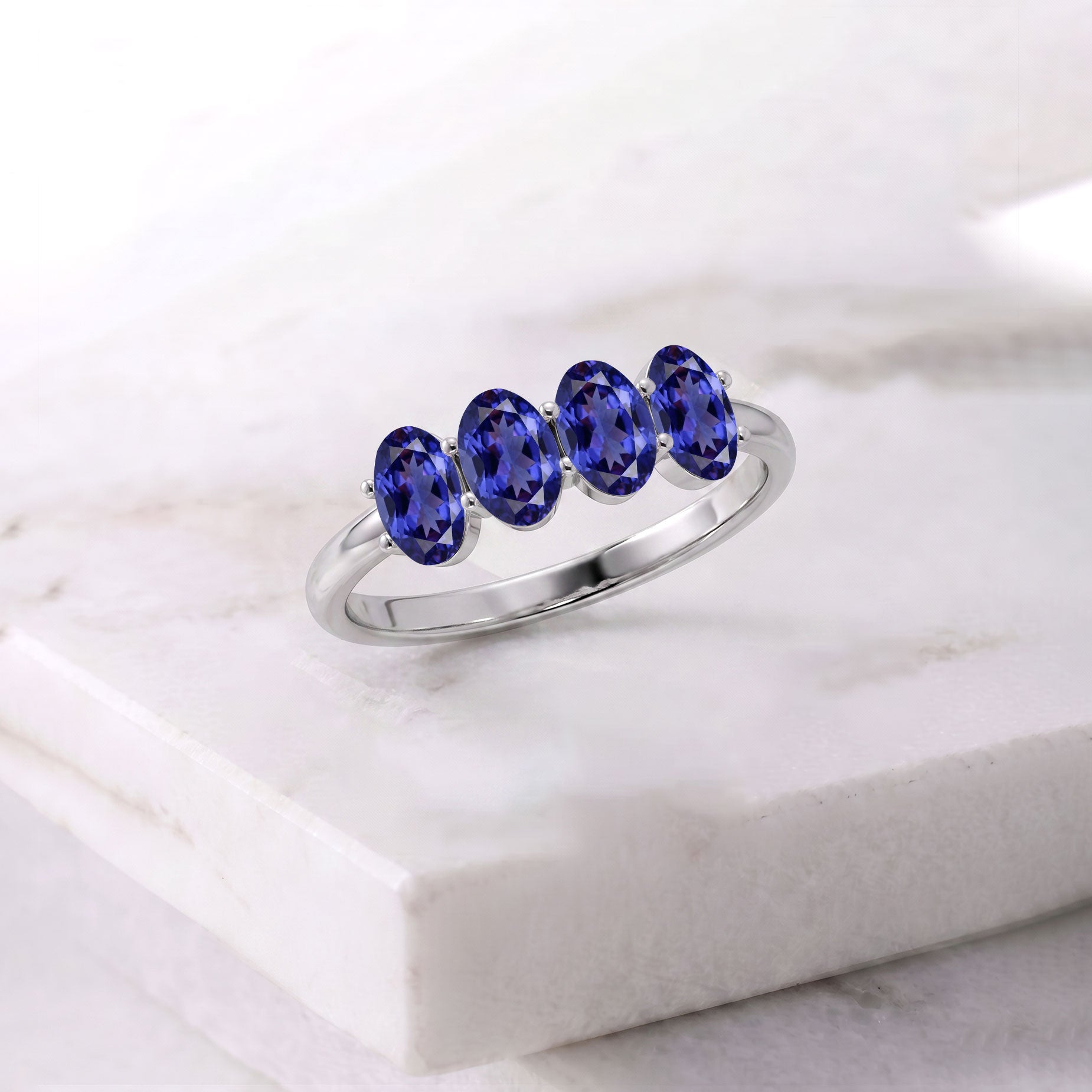 A silver band ring featuring four oval-cut deep blue gemstones, displayed on a white marble block.